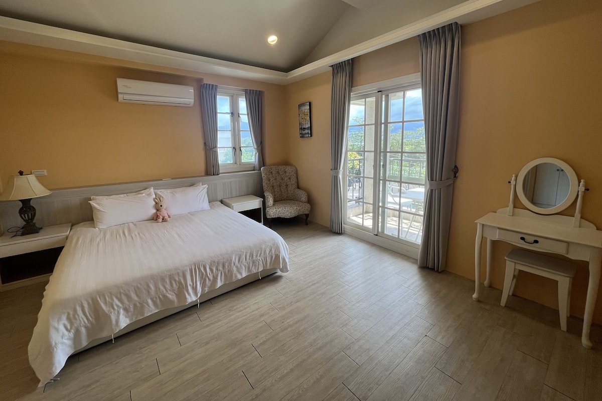 A hotel room with a large bed, a vanity with a mirror, and a chair.