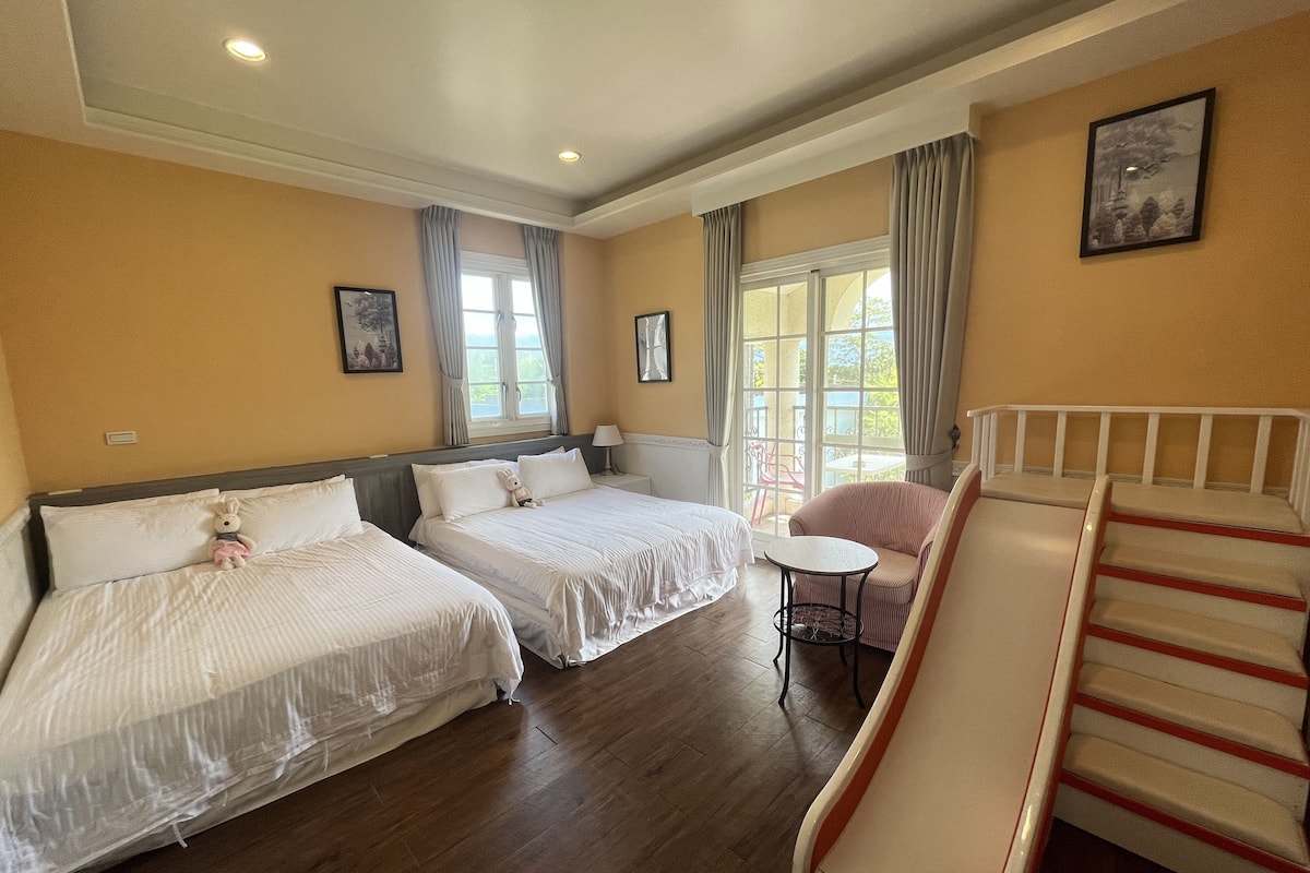 A hotel room with two beds, a small table, a chair, and a staircase.