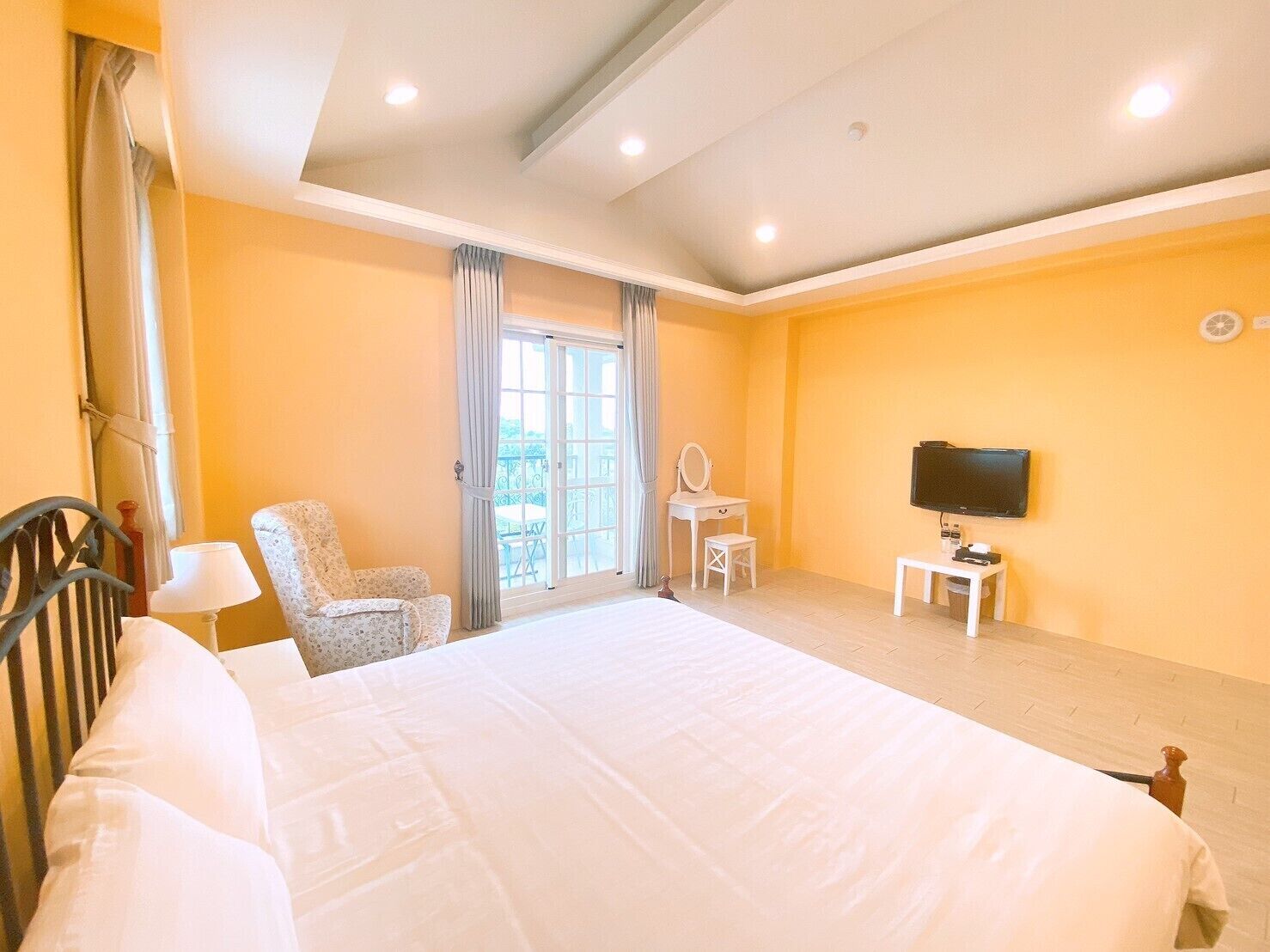 A hotel room with a large bed, a TV, a small table, a chair, and a balcony view.