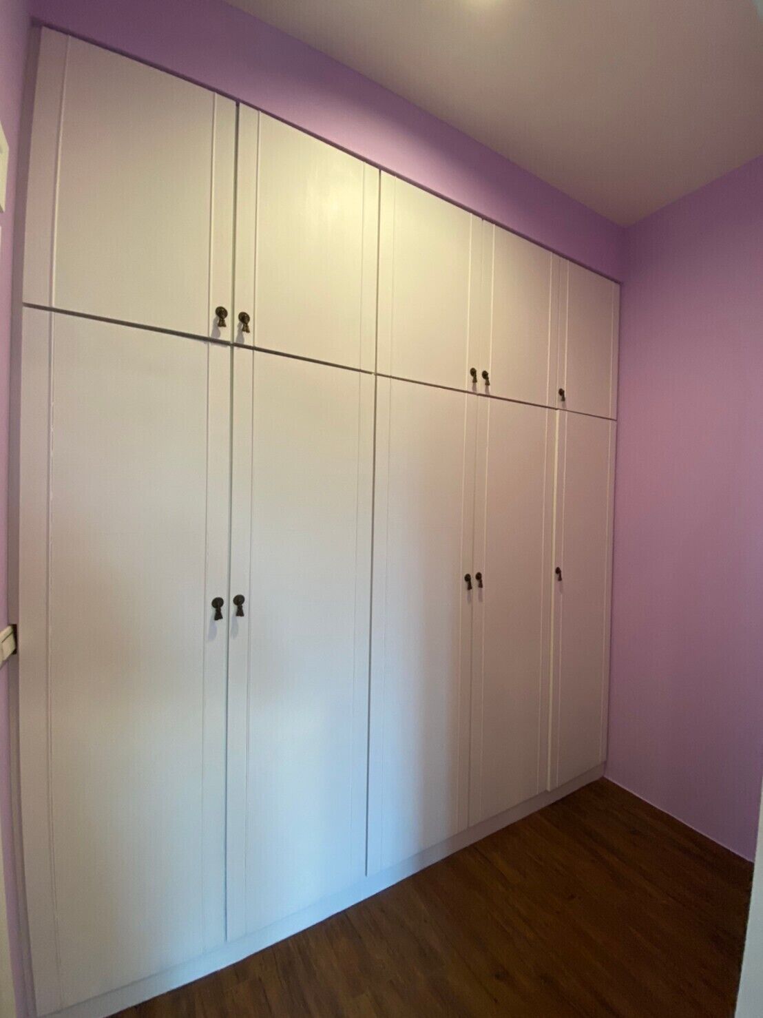 A room with a large white wardrobe, wooden flooring, and purple walls.