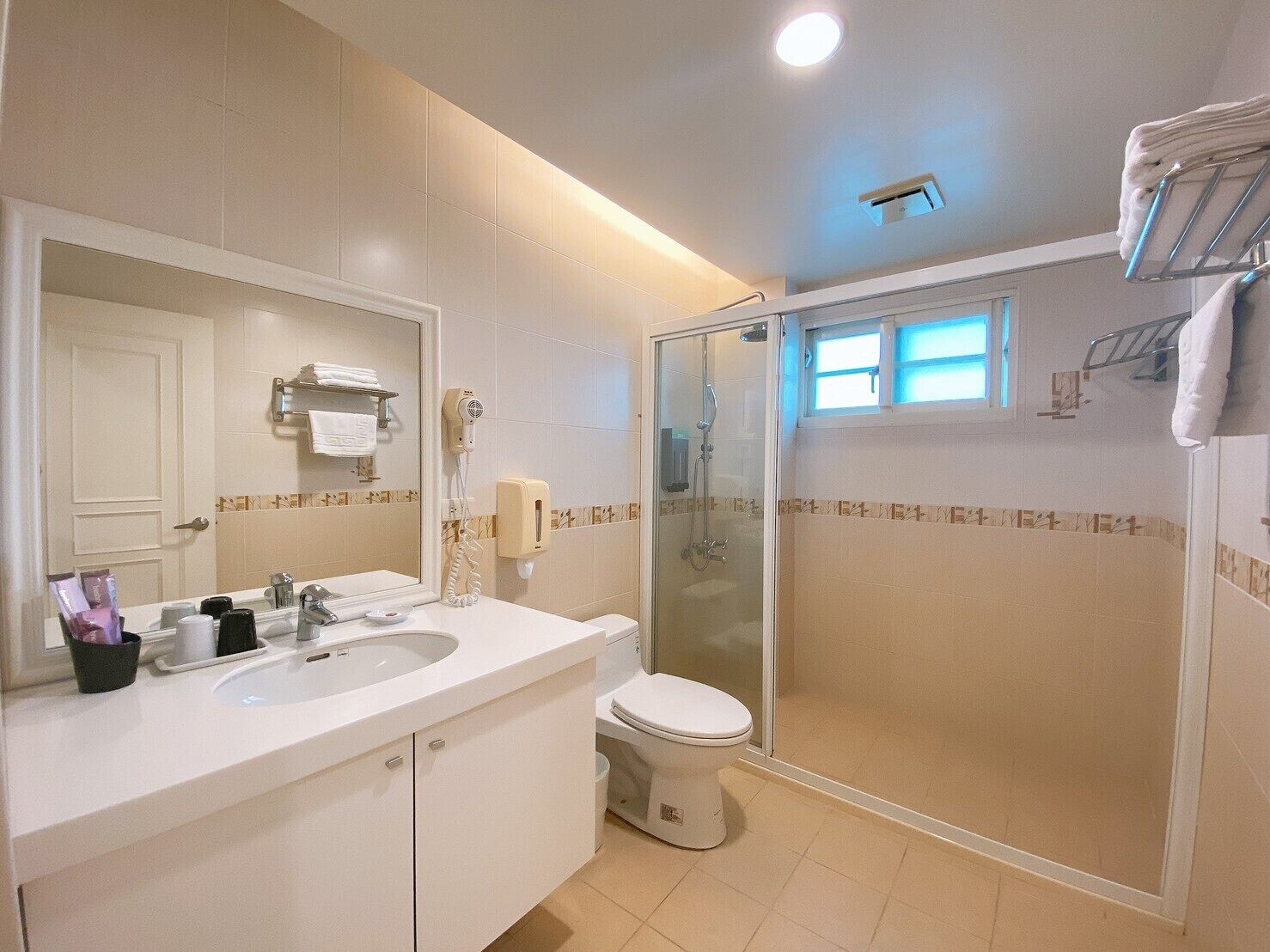 Un baño moderno con lavabo, espejo, inodoro y ducha con mampara de vidrio.