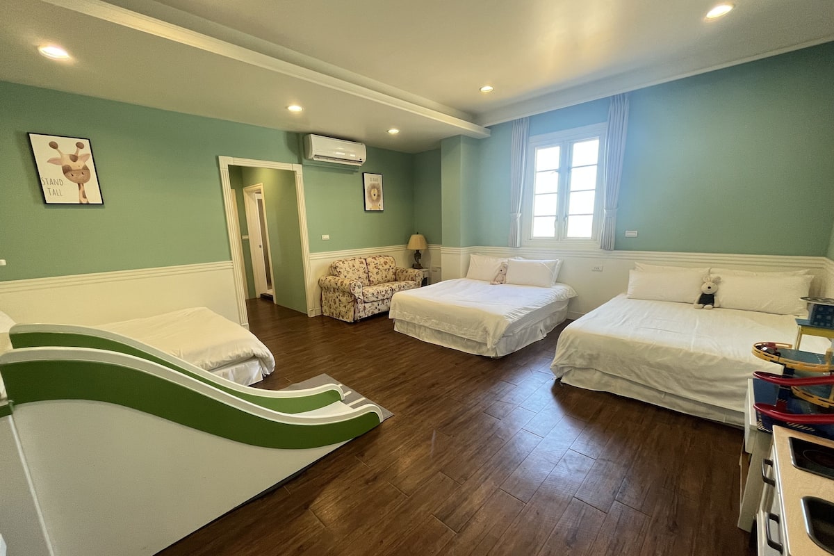 A room with three beds, a sofa, a kitchenette, and a window with curtains.