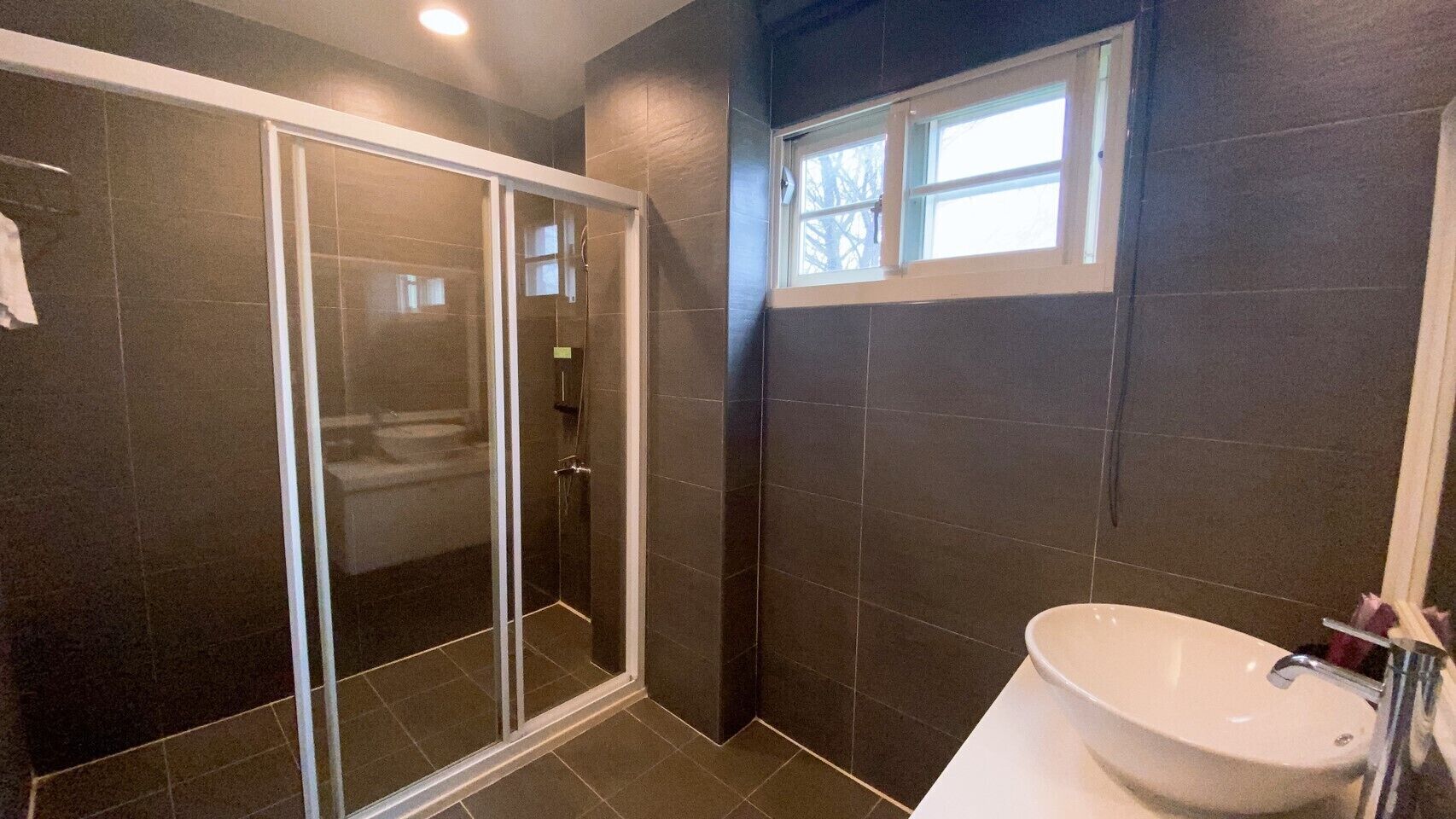 A bathroom with a glass-enclosed shower, a large sink, and a window above the sink.