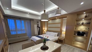 Ett hotellrum med en säng, sängbord, ett skrivbord, en stol, ett litet pentry och ett fönster med gardiner.