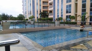 A swimming pool with a tiled deck, surrounded by a fence and palm trees. - Fantastic Step to the Venice (Taguig)