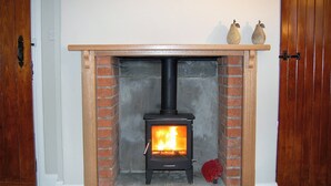 Una estufa de leña con chimenea de ladrillo, repisa de madera y dos jarrones decorativos encima.