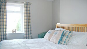Un dormitorio con cama, ventana con cortinas y cabecero.
