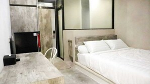 A compact hotel room with a single bed, a small table, a chair, and a built-in desk. - D'Paragon Beo (Depok)