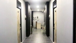 A narrow hallway with doors on both sides, a trash bin, and a chair in the center. - D'Paragon Beo (Depok)