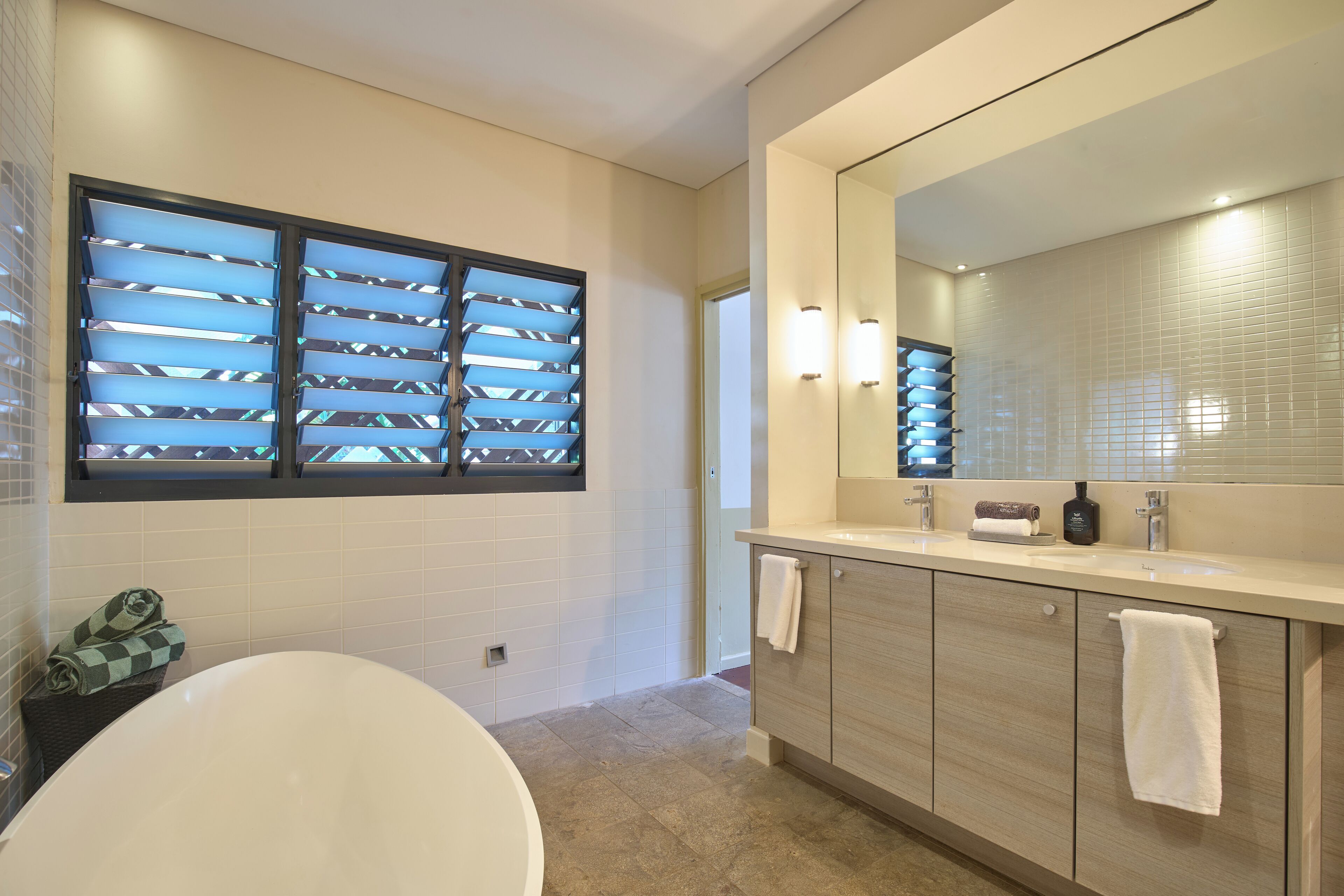 A modern bathroom with a large mirror, a bathtub, and a vanity with a sink.