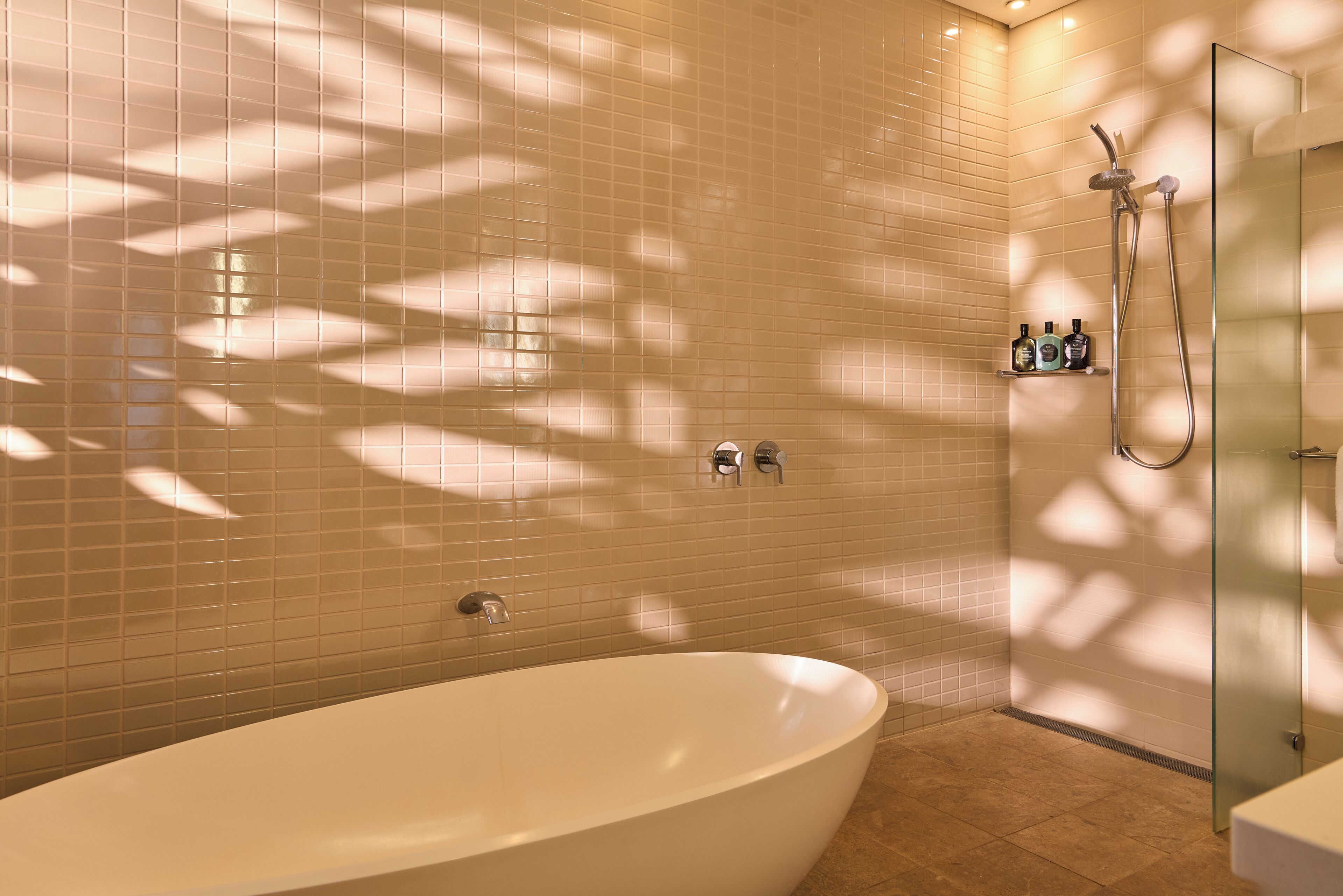 A modern bathroom with a freestanding bathtub, a glass shower enclosure, and a tiled wall.