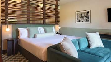 Une chambre d’hôtel avec un lit, un canapé, un sol à carreaux, une tête de lit en bois et un tableau encadré au mur.
