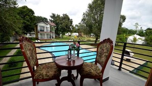 A balcony with two chairs and a table, overlooking a swimming pool and a house. - The Lion Kingdom Sigiriya (Dambulla)