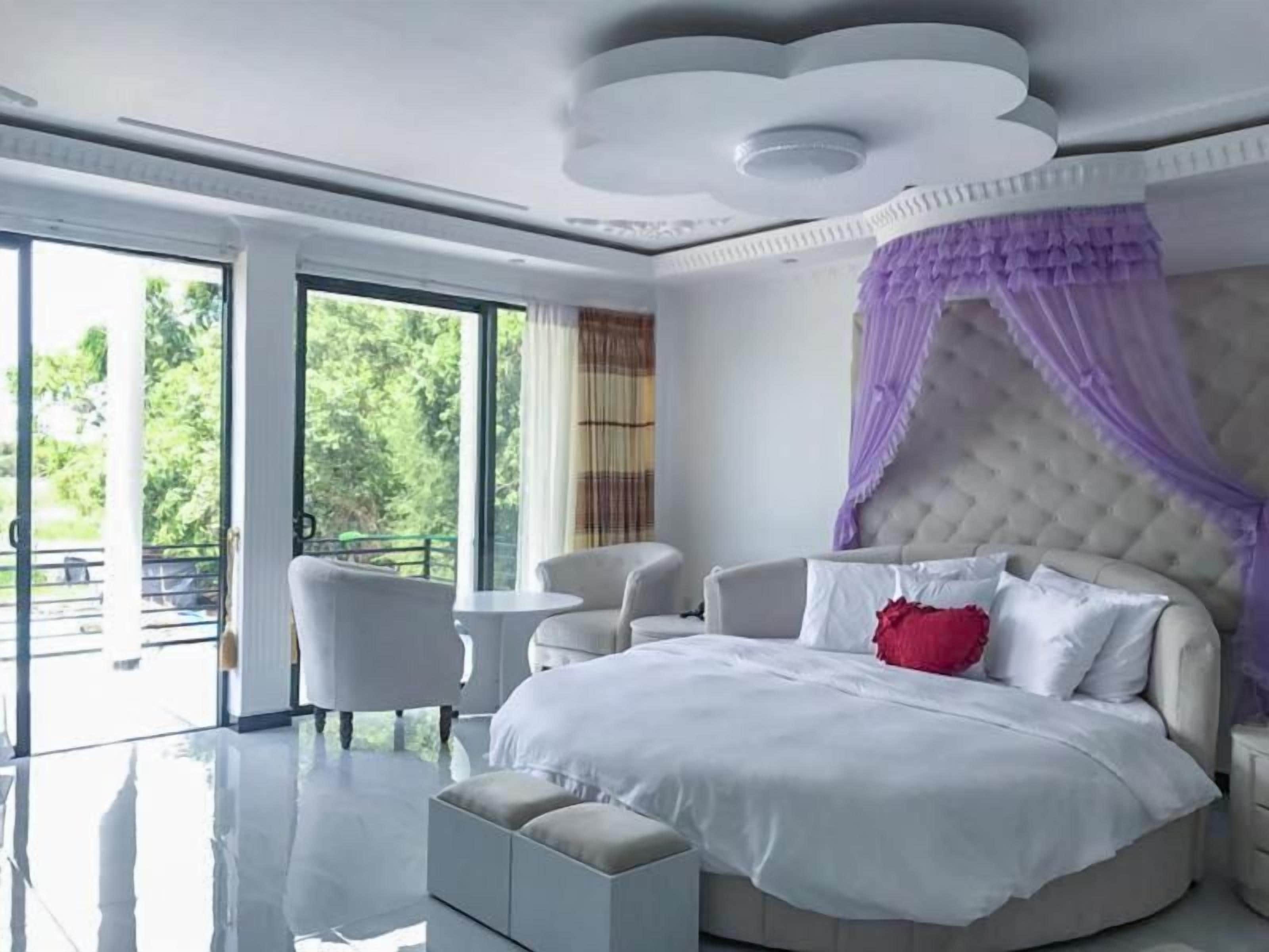 Ein modernes Schlafzimmer mit einem großen Bett, einer runden Sitzecke und Blick auf Grünflächen.