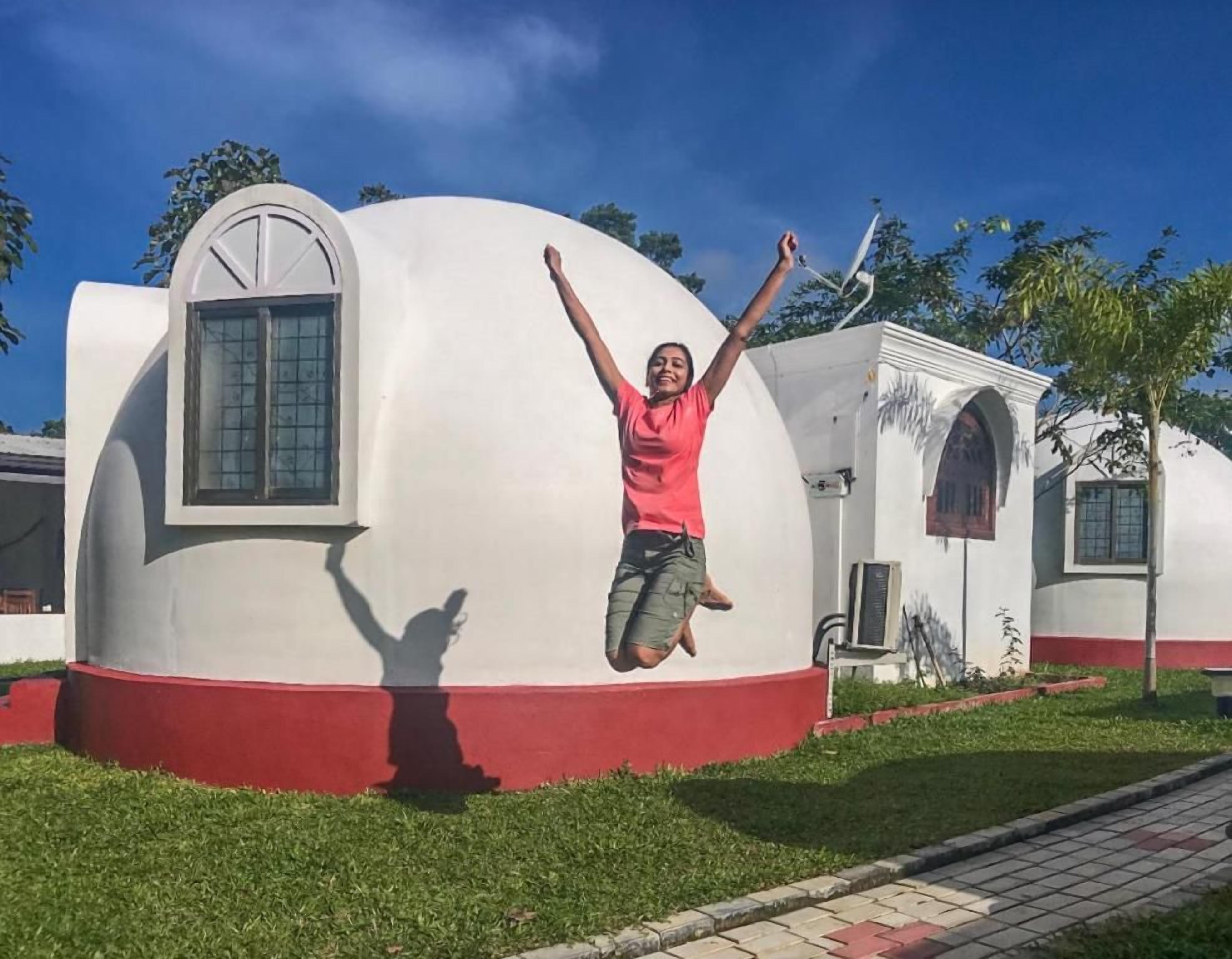 A person jumping in front of a white and red building with a curved facade and a window.