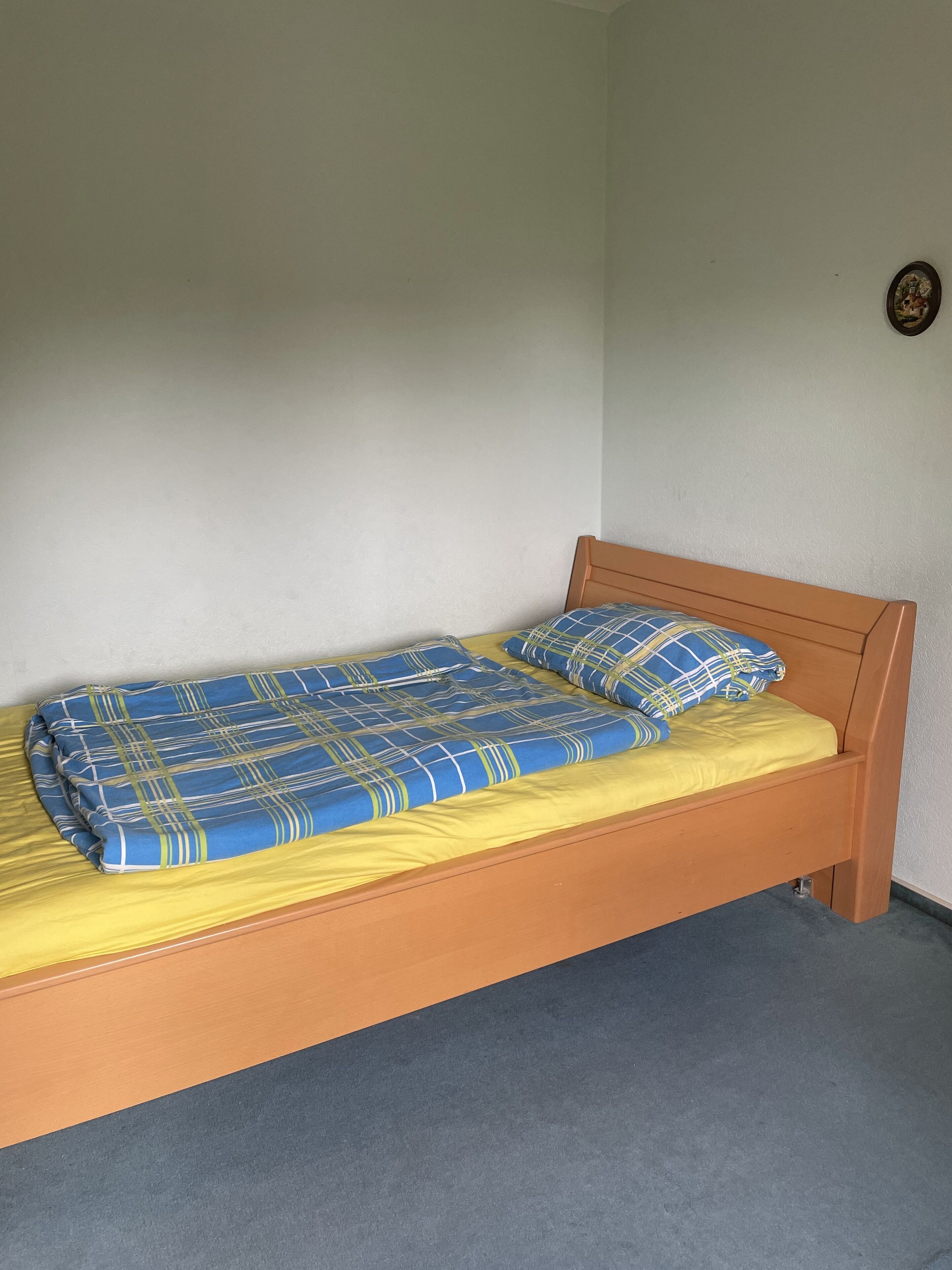 Ein Einzelbett mit Holzrahmen, einer blauen und gelben Tagesdecke und passenden Kissen.