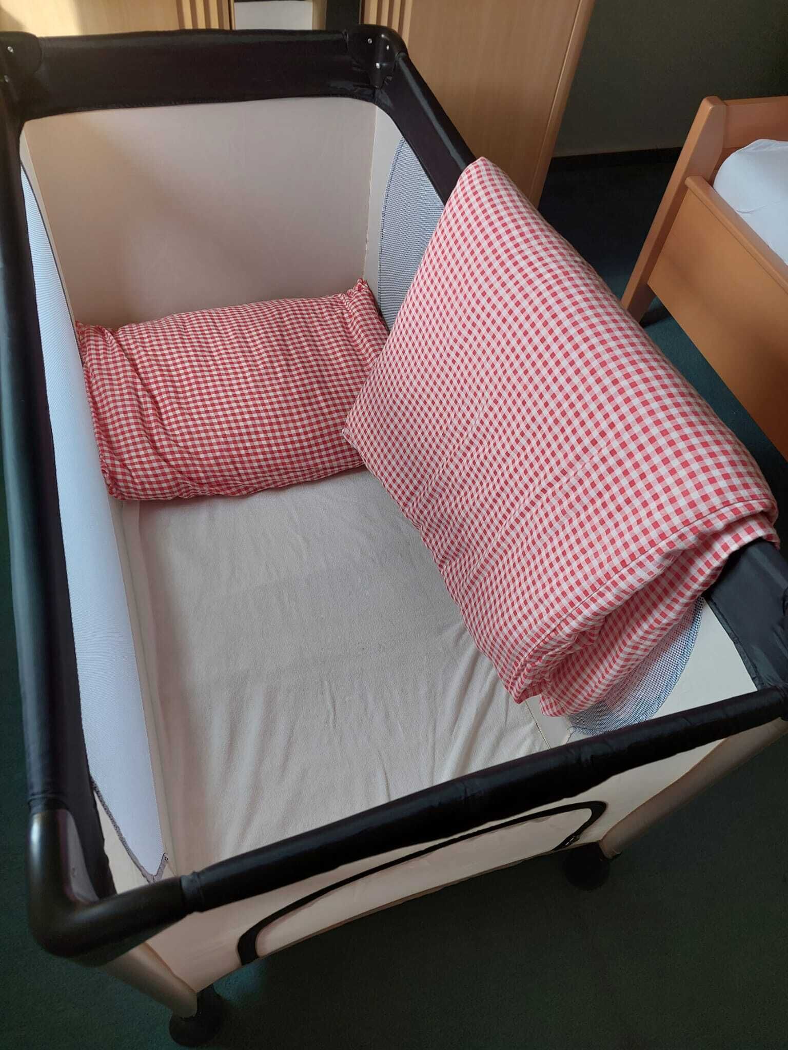 A baby crib with a white mattress and two red and white checkered blankets.