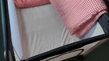 A baby crib with a white mattress and two red and white checkered blankets.