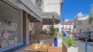 An outdoor dining area with wicker furniture, a table with breakfast items, and a planter with green plants. - Azur Hotel (Balaruc-les-Bains)