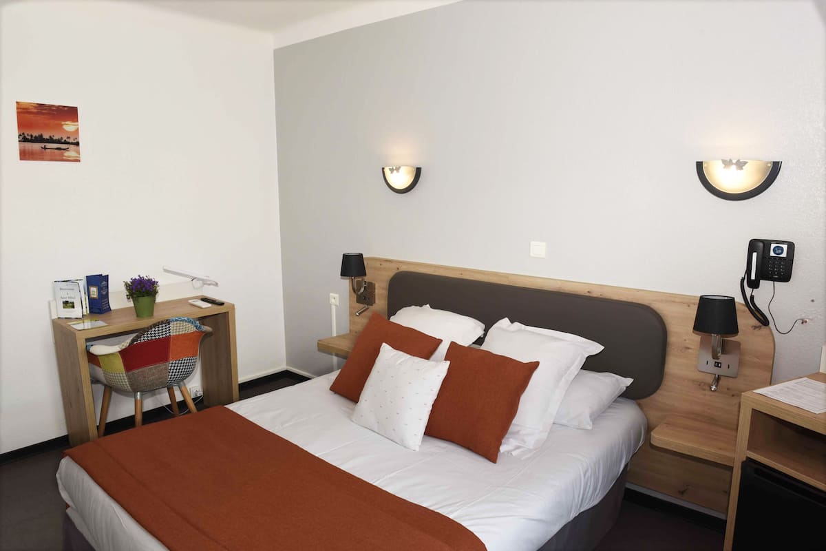 A neatly arranged hotel room with a bed, bedside tables, a desk, and a chair.