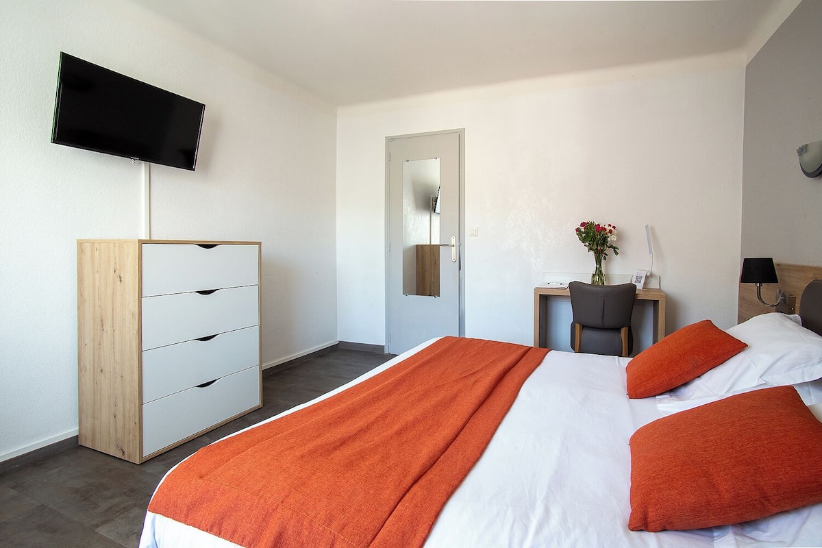 A hotel room with a bed, a desk, a chair, a wardrobe, and a flat-screen TV mounted on the wall.