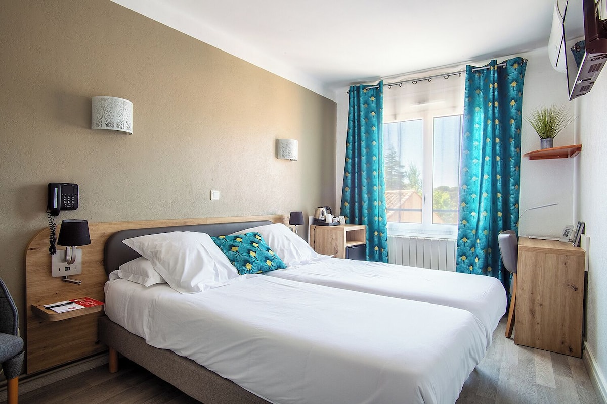 A hotel room with two beds, a desk, a chair, a phone, a lamp, and a window with curtains.