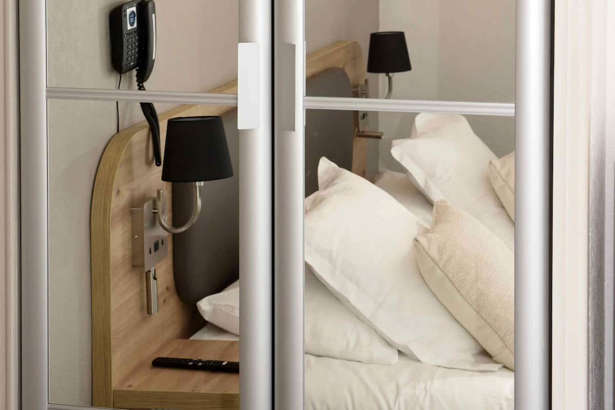 A hotel room with a bed, a bedside lamp, a phone, and a wall-mounted light fixture.