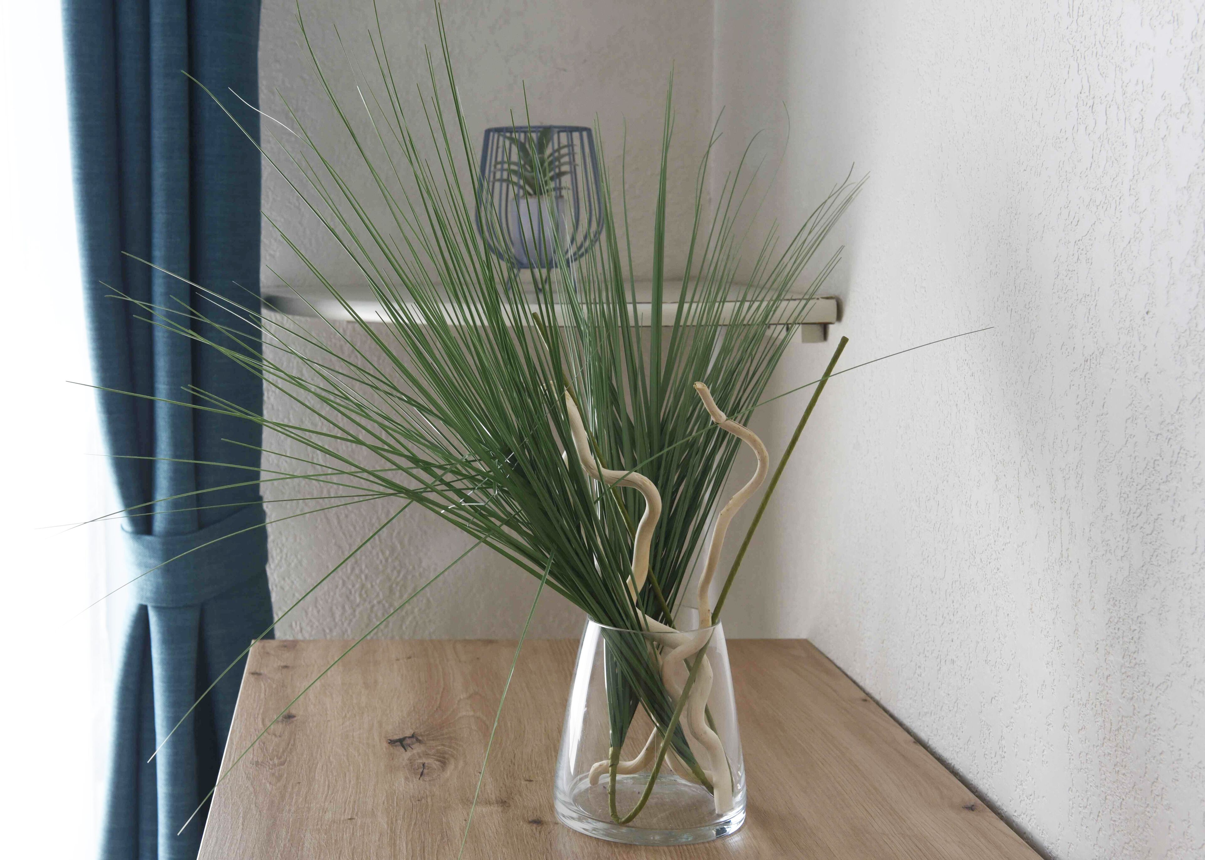 Eine transparente Glasvase mit Grünpflanzen auf einem Holztisch.