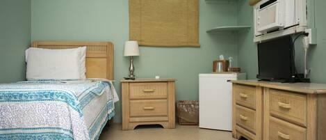 A bedroom with a bed, bedside table, lamp, dresser, and a small white appliance.