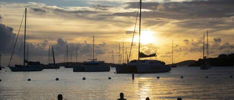 A marina with boats and people in the water during sunset.