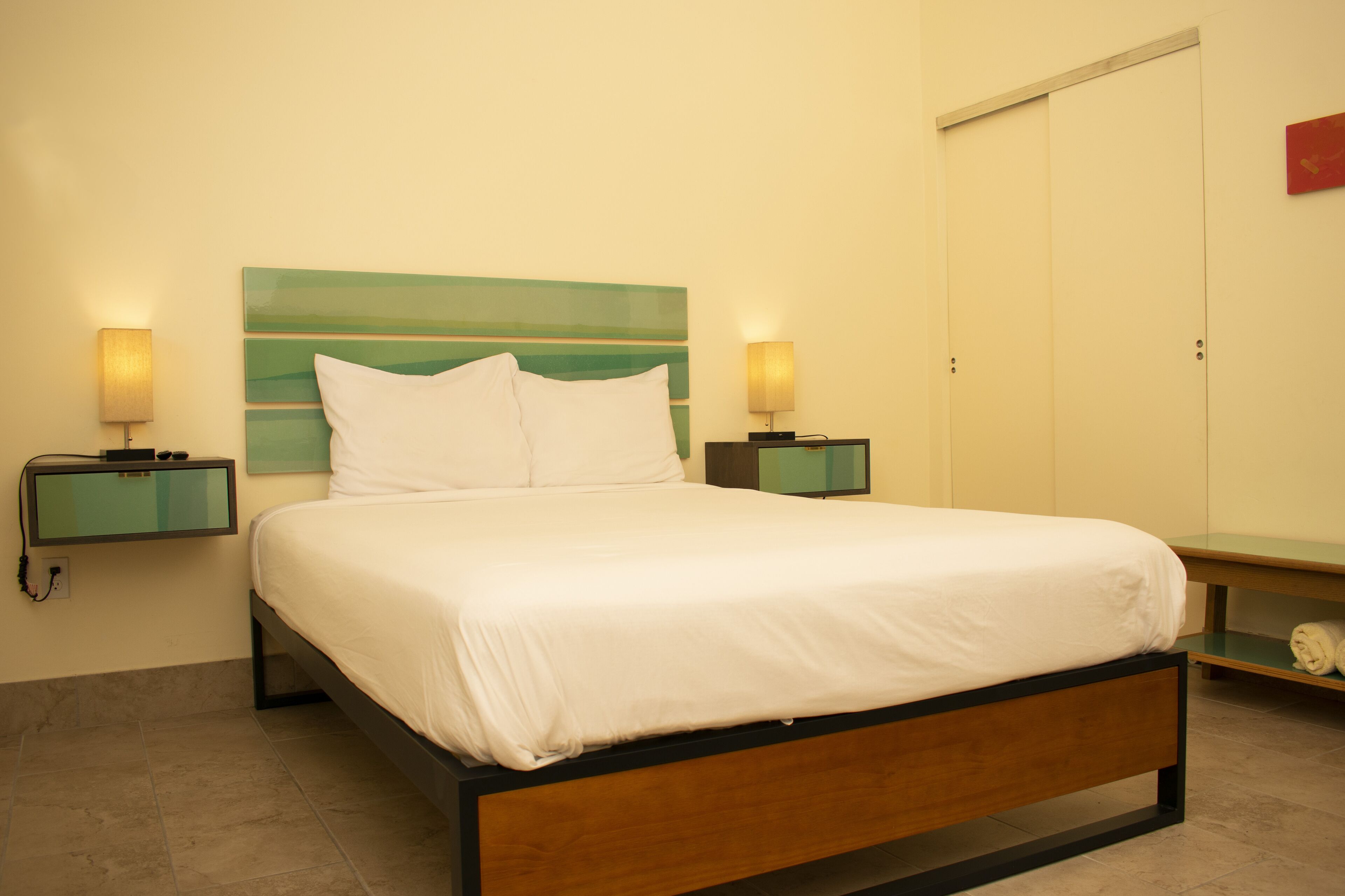 A neatly made bed with white linens, two bedside tables with lamps, a green headboard, and a wardrobe with a sliding door.