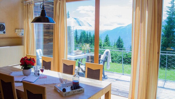 A dining area with a wooden table, chairs, and a view of mountains through large windows.