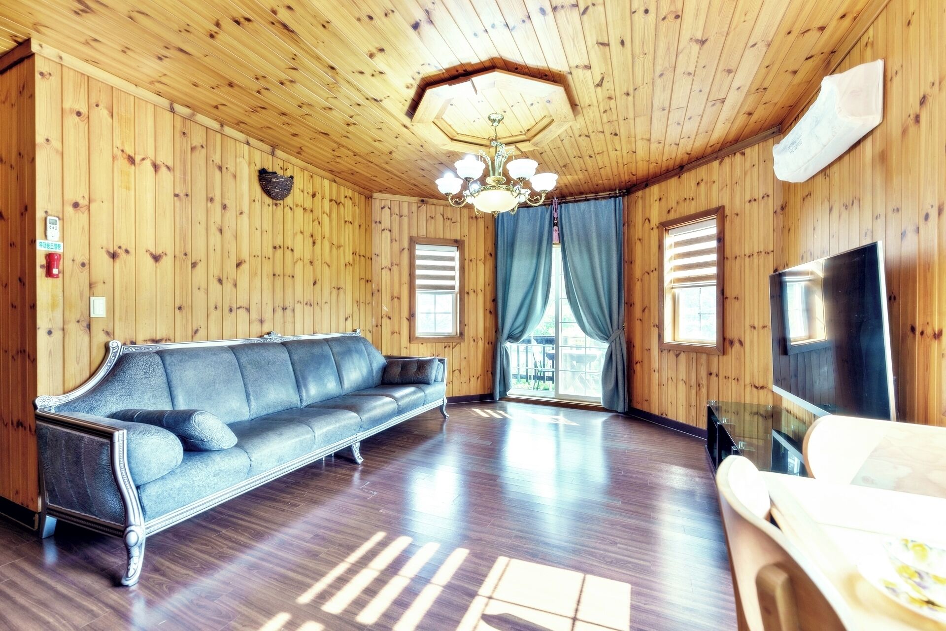 A wooden-paneled room with a leather sofa, a chandelier, and a television.