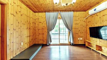 A room with wooden walls, a large window with curtains, a wooden bench, and a flat-screen TV.