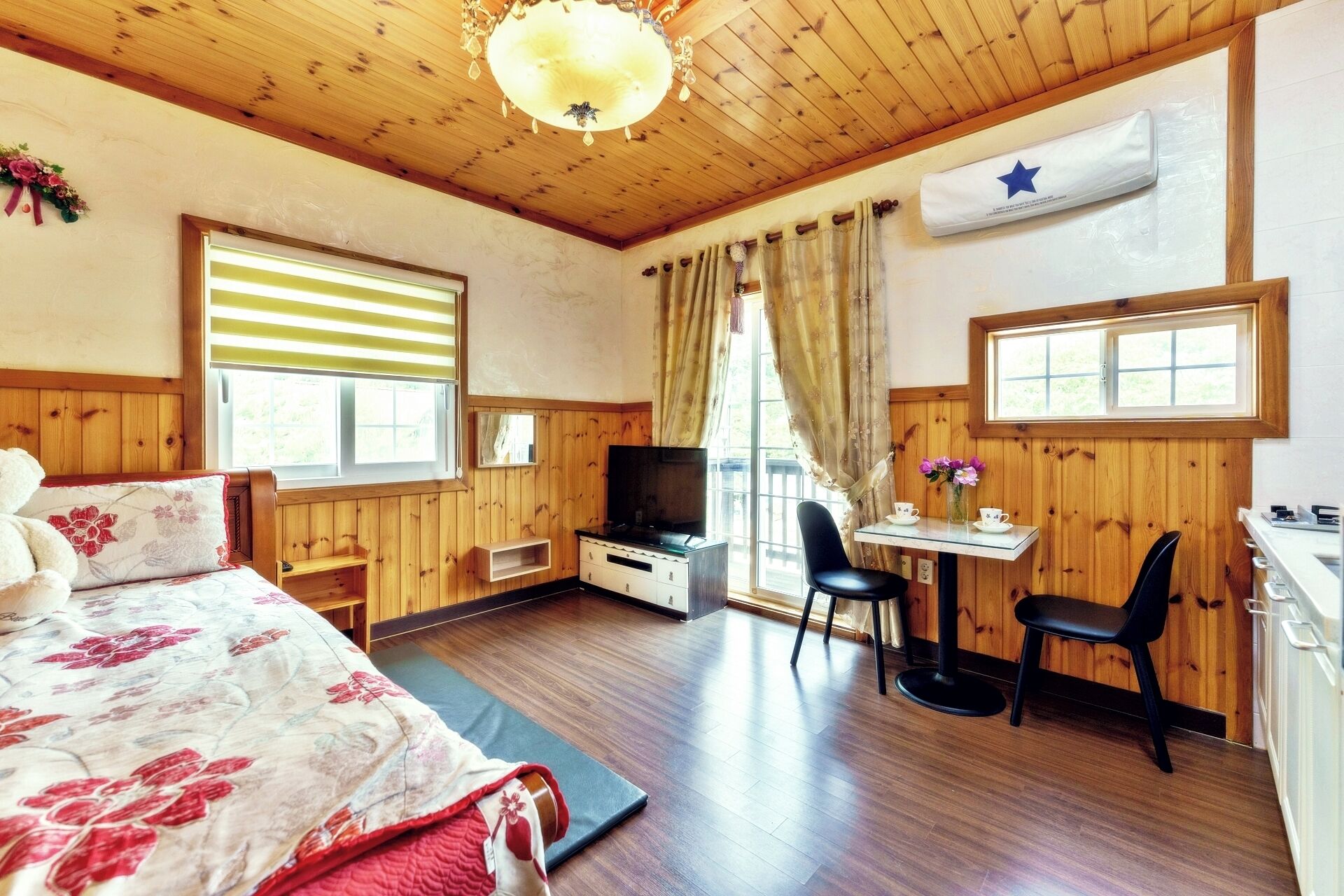 A cozy room with a bed, a desk, a chair, a television, and a flag on the wall.