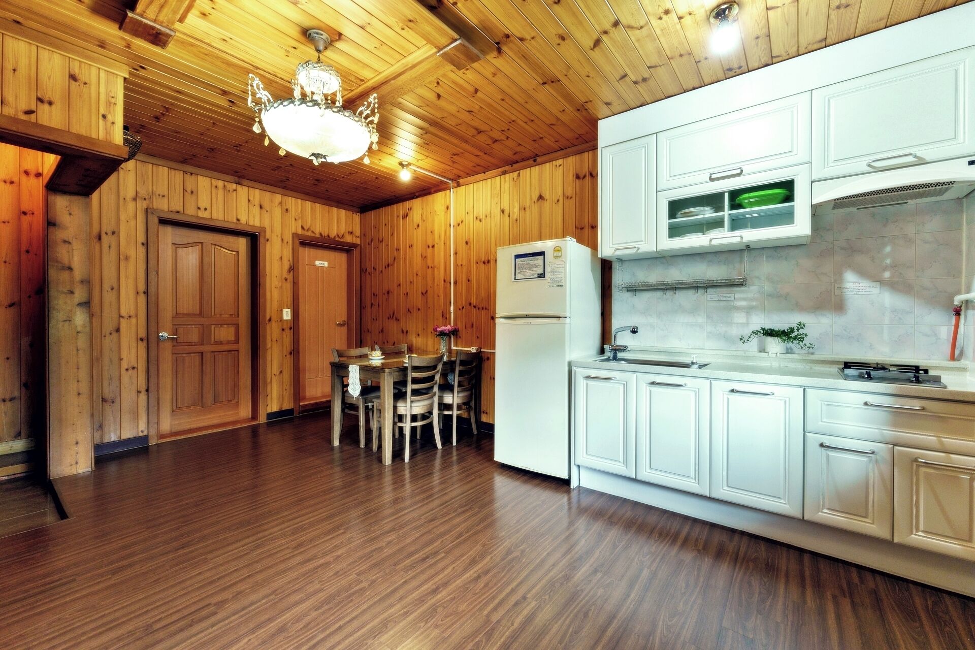 A wooden-paneled room with a dining table and chairs, a refrigerator, and white cabinets.