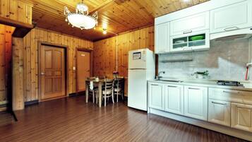 A wooden-paneled room with a dining table and chairs, a refrigerator, and white cabinets.