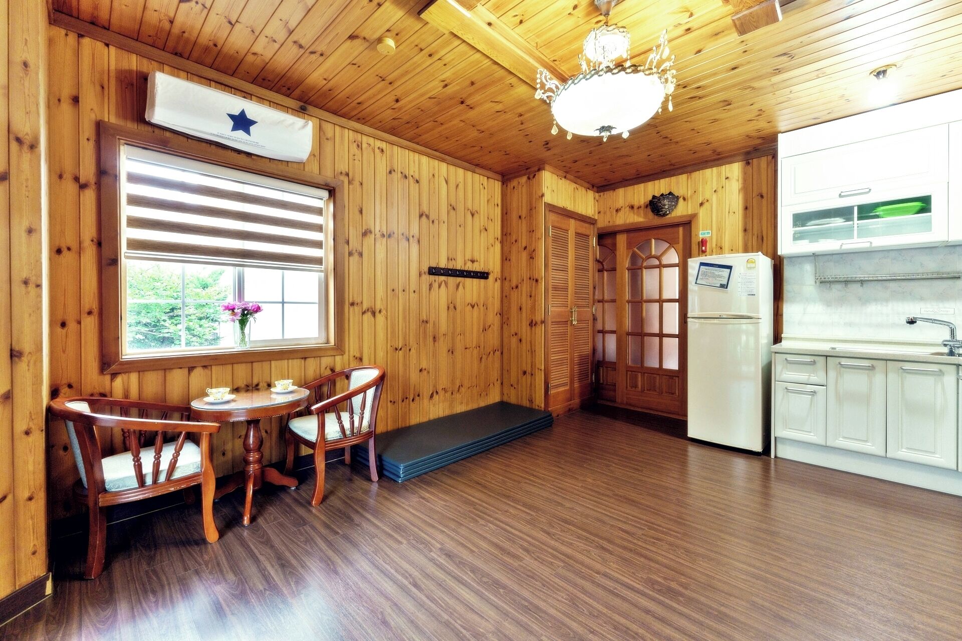A wooden interior with a dining table, chairs, a refrigerator, and a kitchen area.