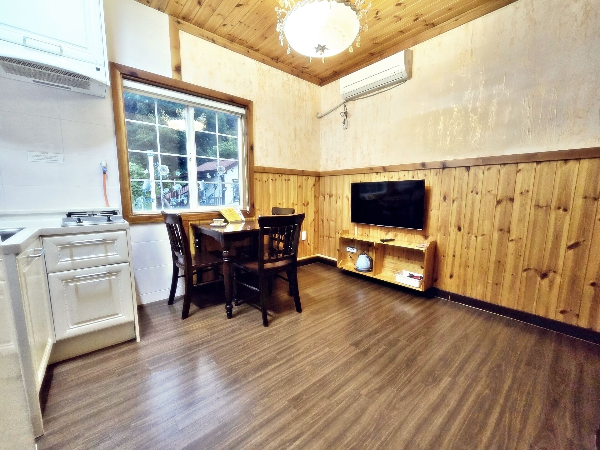 A wooden-paneled room with a dining table, chairs, a TV, and a kitchenette.
