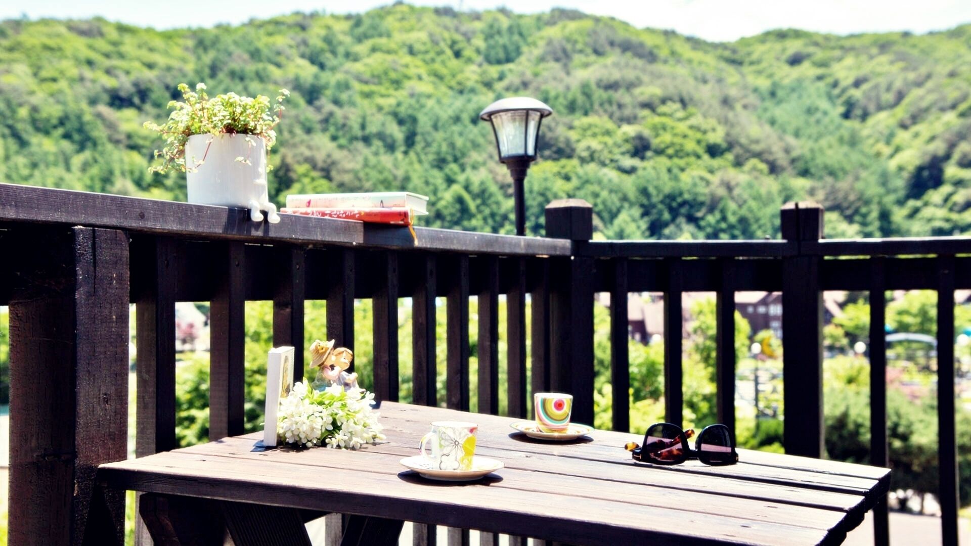 A wooden deck with a table set for tea, a potted plant, and sunglasses.
