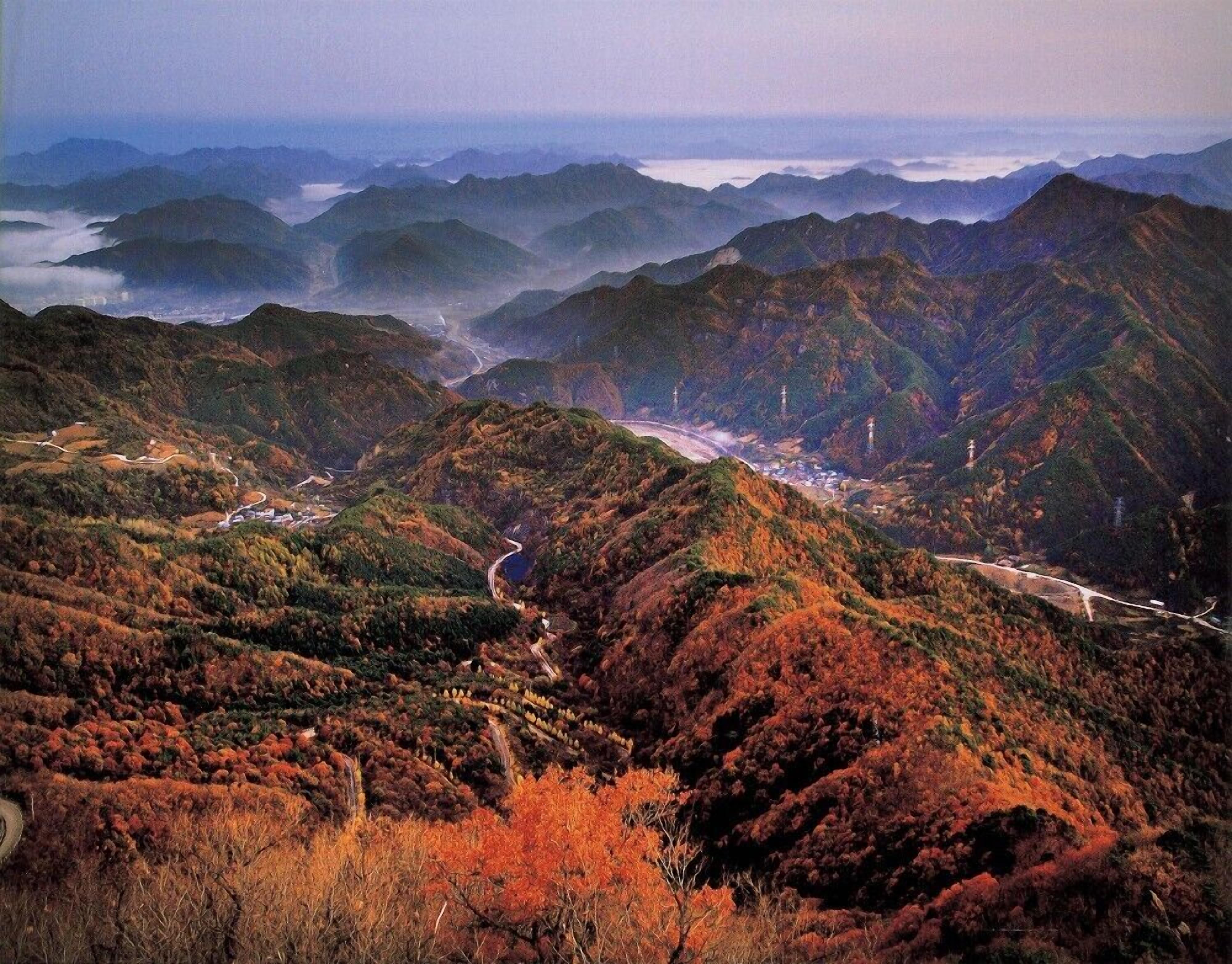 A mountainous landscape with winding roads and a distant view of a town.