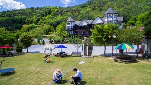 Een groot huis met een toren, omringd door een gazon met picknicktafels en parasols.