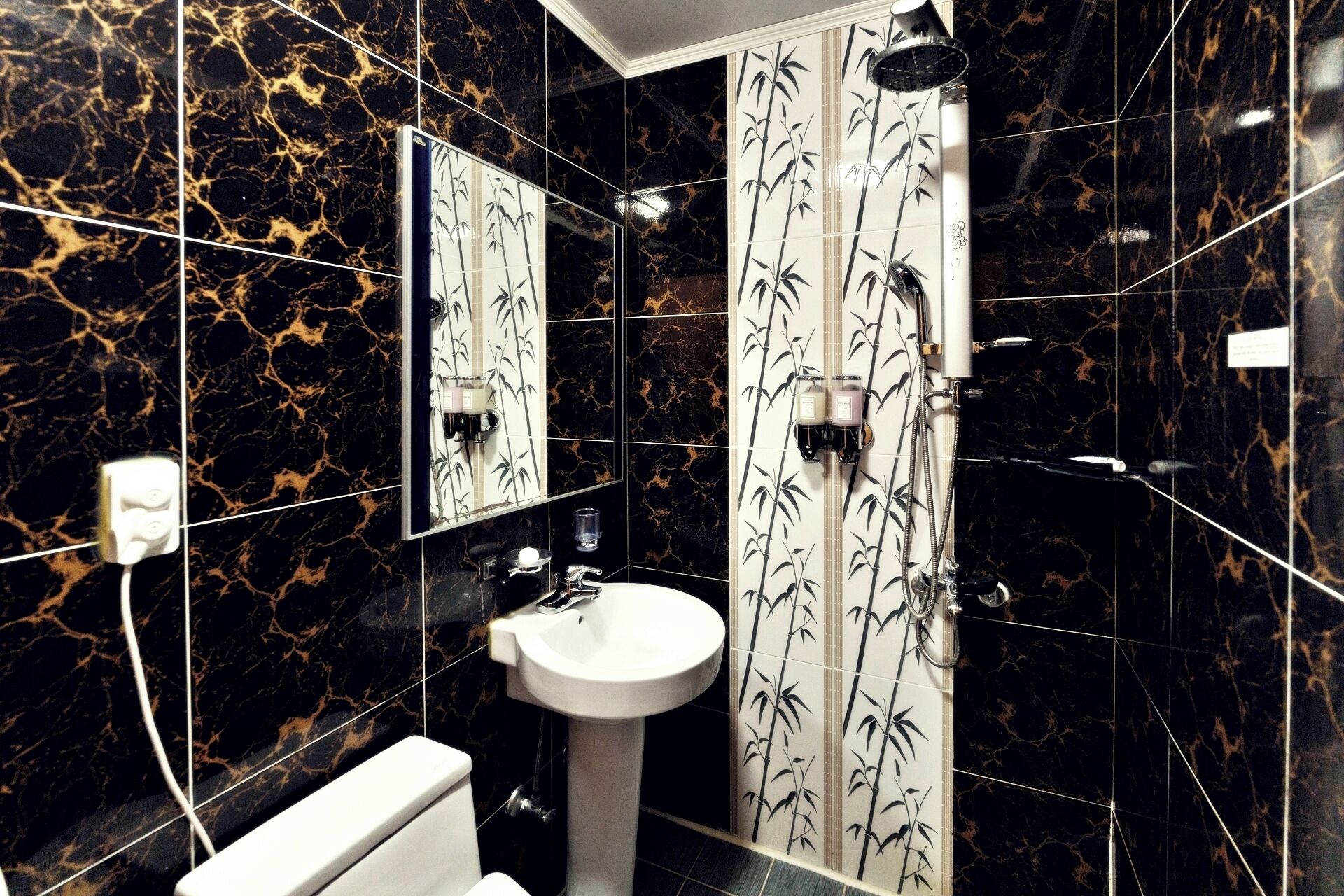 Un bagno con WC, lavandino e doccia. Le pareti presentano un motivo marmorizzato nero e oro.