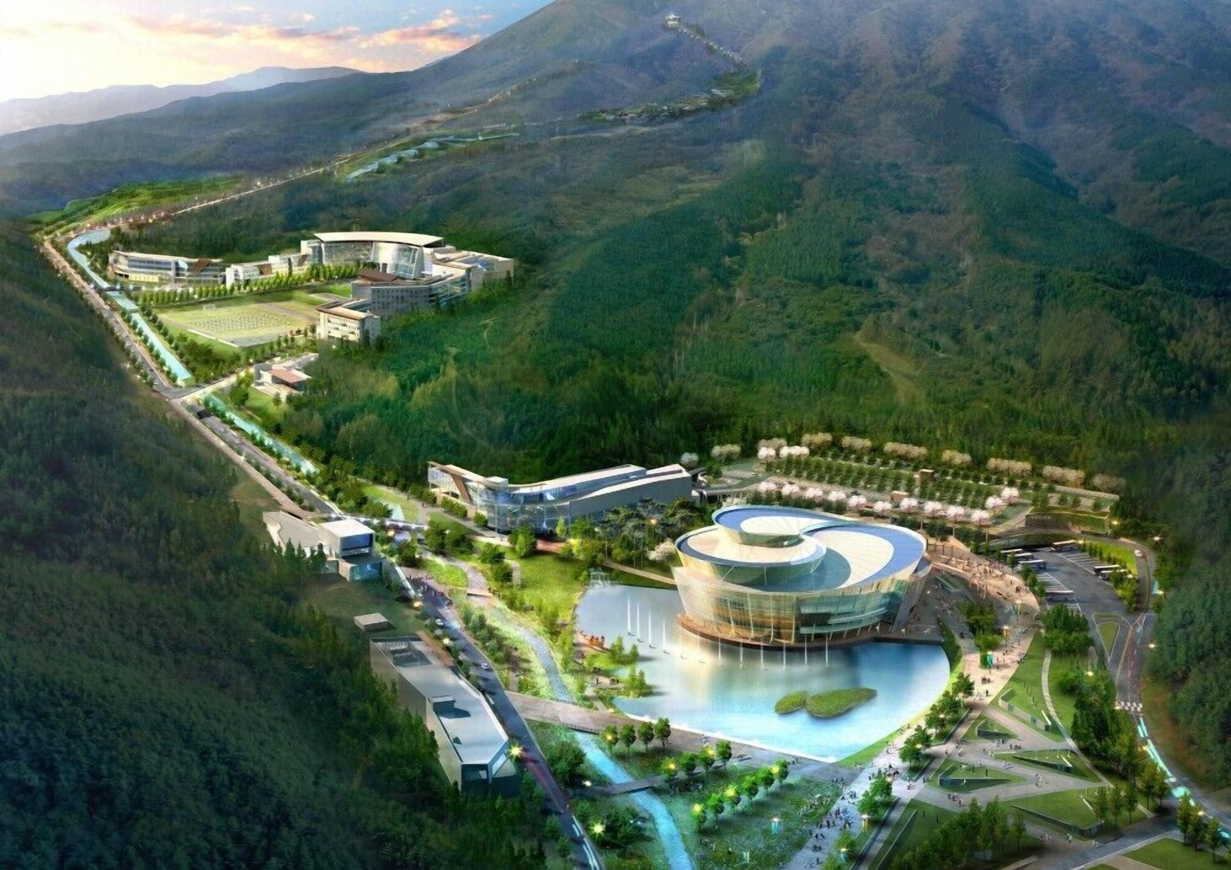 Vista aerea di un resort moderno con un edificio centrale circolare, edifici collegati e un'area paesaggistica con un elemento d'acqua.