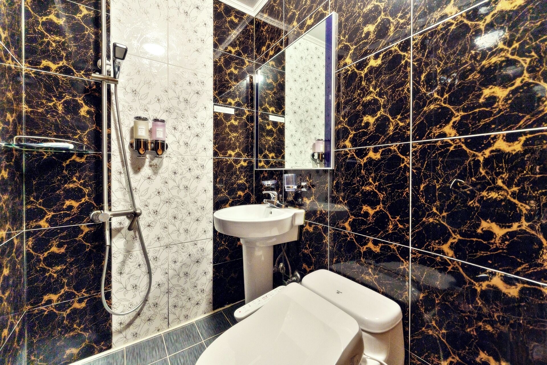 Casa de banho com azulejos de mármore preto e dourado, uma sanita branca, uma pia e um chuveiro com cabine de vidro.