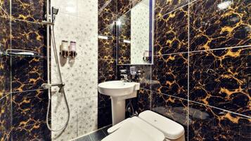 Casa de banho com azulejos de mármore preto e dourado, uma sanita branca, uma pia e um chuveiro com cabine de vidro.