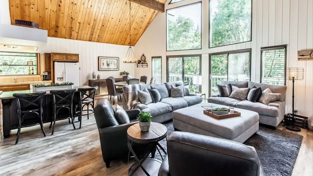 A spacious living area with a large grey sectional sofa, a dining table with chairs, and a kitchen area with a refrigerator and wooden cabinets. - SPACIOUS BLUE JAY CABIN WITH VAULTED CEILINGS! (Lake Arrowhead)