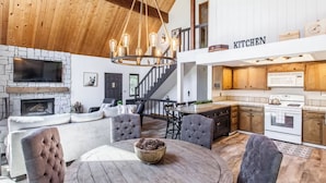 A spacious living room with a fireplace, a dining area with a round table, and a kitchen area with wooden cabinets and a microwave. - SPACIOUS BLUE JAY CABIN WITH VAULTED CEILINGS! (Lake Arrowhead)