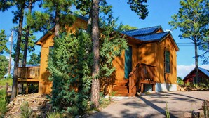 A wooden cabin with a porch, surrounded by trees. - Mountain Majesty (Ruidoso)