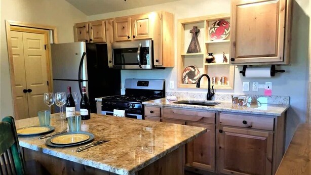A kitchen with wooden cabinets, a stainless steel refrigerator, a microwave, a stove, and a granite countertop. - Mountain Majesty (Ruidoso)
